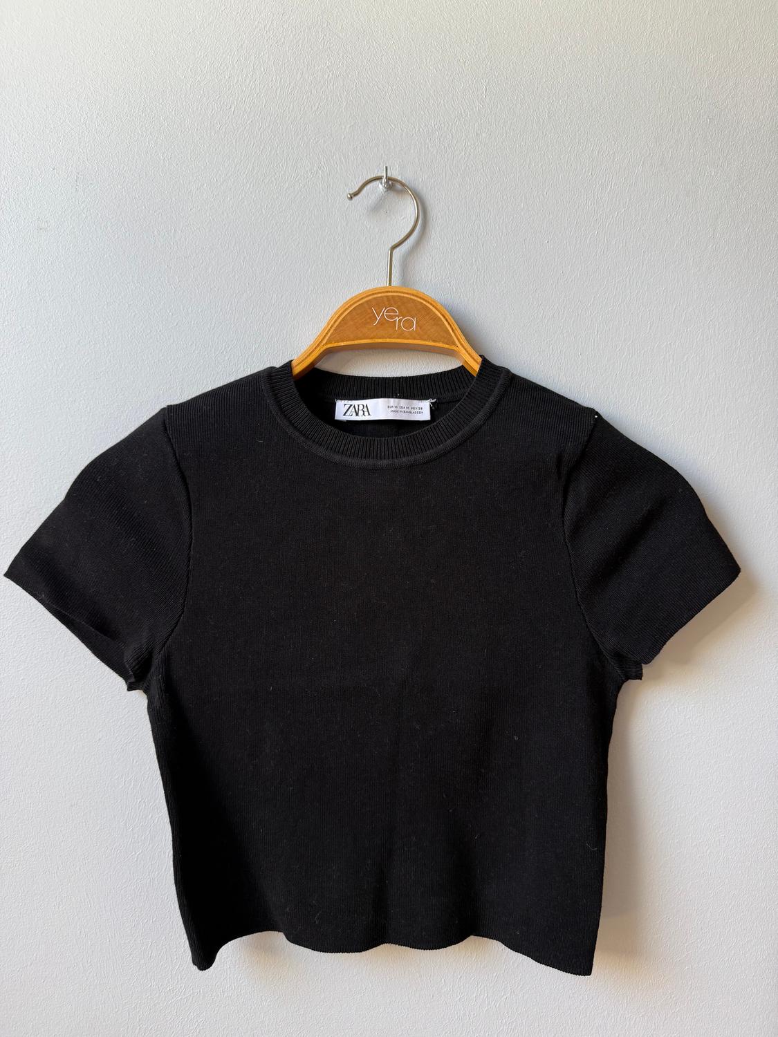 Black short-sleeved T-shirt hanging on a wooden hanger with the brand "yera", visible ZARA tag. White background.