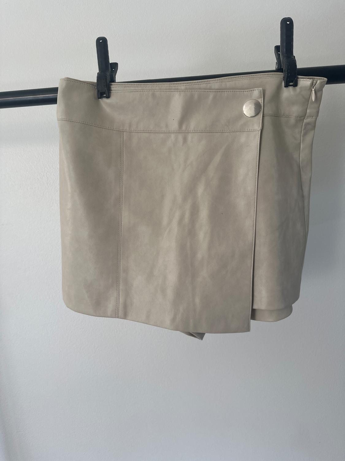 Beige mini skirt hanging on a black hanger, with a decorative silver button on the top right. Plain white background.