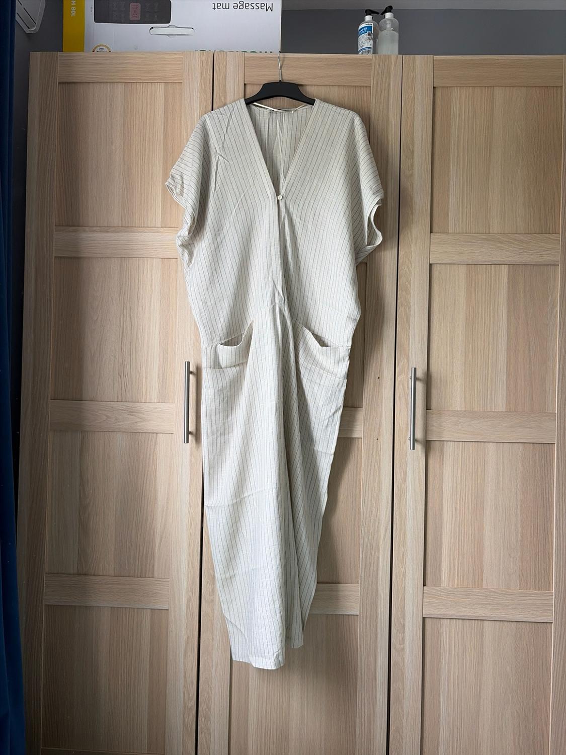 Loose-fitting striped jumpsuit with a V-neck hanging in a wooden wardrobe in a casual setting. The text 'Massage mat' appears at the top.