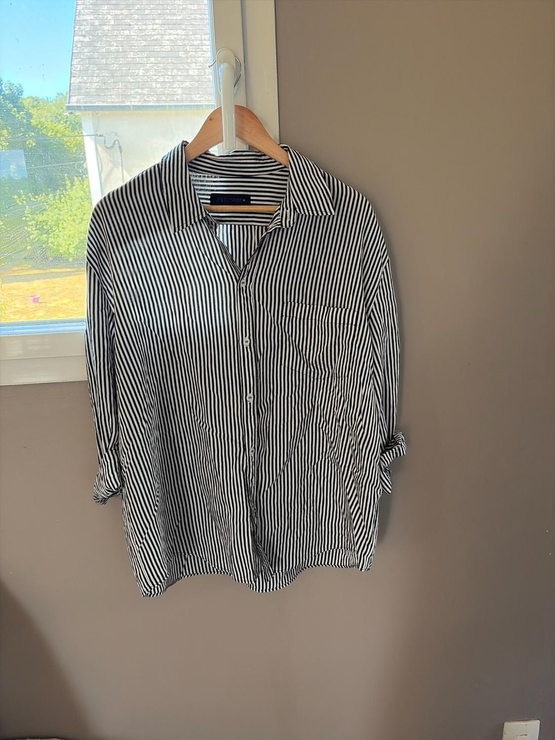 Black and white striped shirt hanging on a wooden hanger on a window handle, with natural light and a view outside.