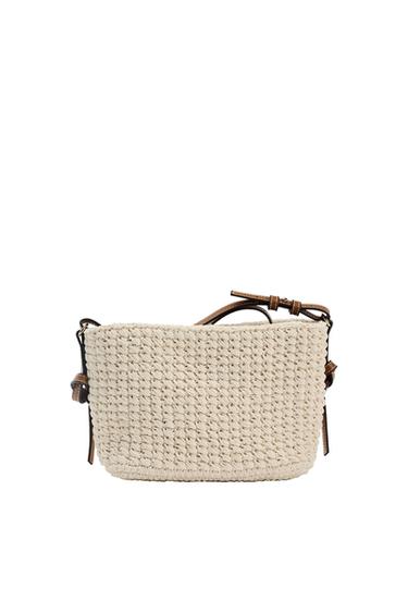Beige woven bag with an adjustable brown leather strap on a white background. Simple and elegant design.
