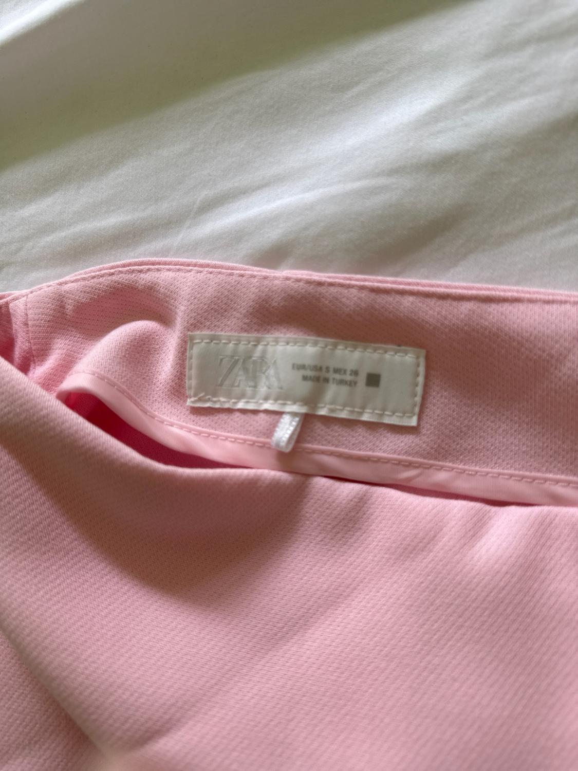 Pink garment on white fabric showing its inner label with the text ZARA EUR/USA S MEX 26 MADE IN TURKEY.