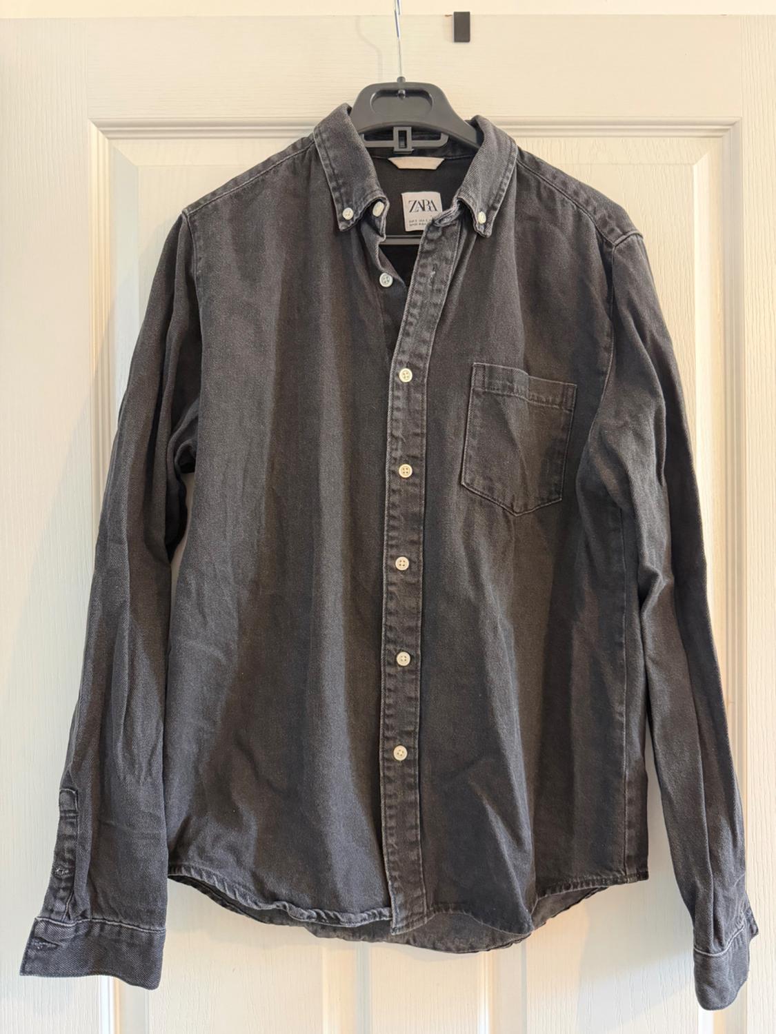 Grey long-sleeved shirt hanging on a black hanger, with white buttons and a chest pocket. Visible label: "ZARA".