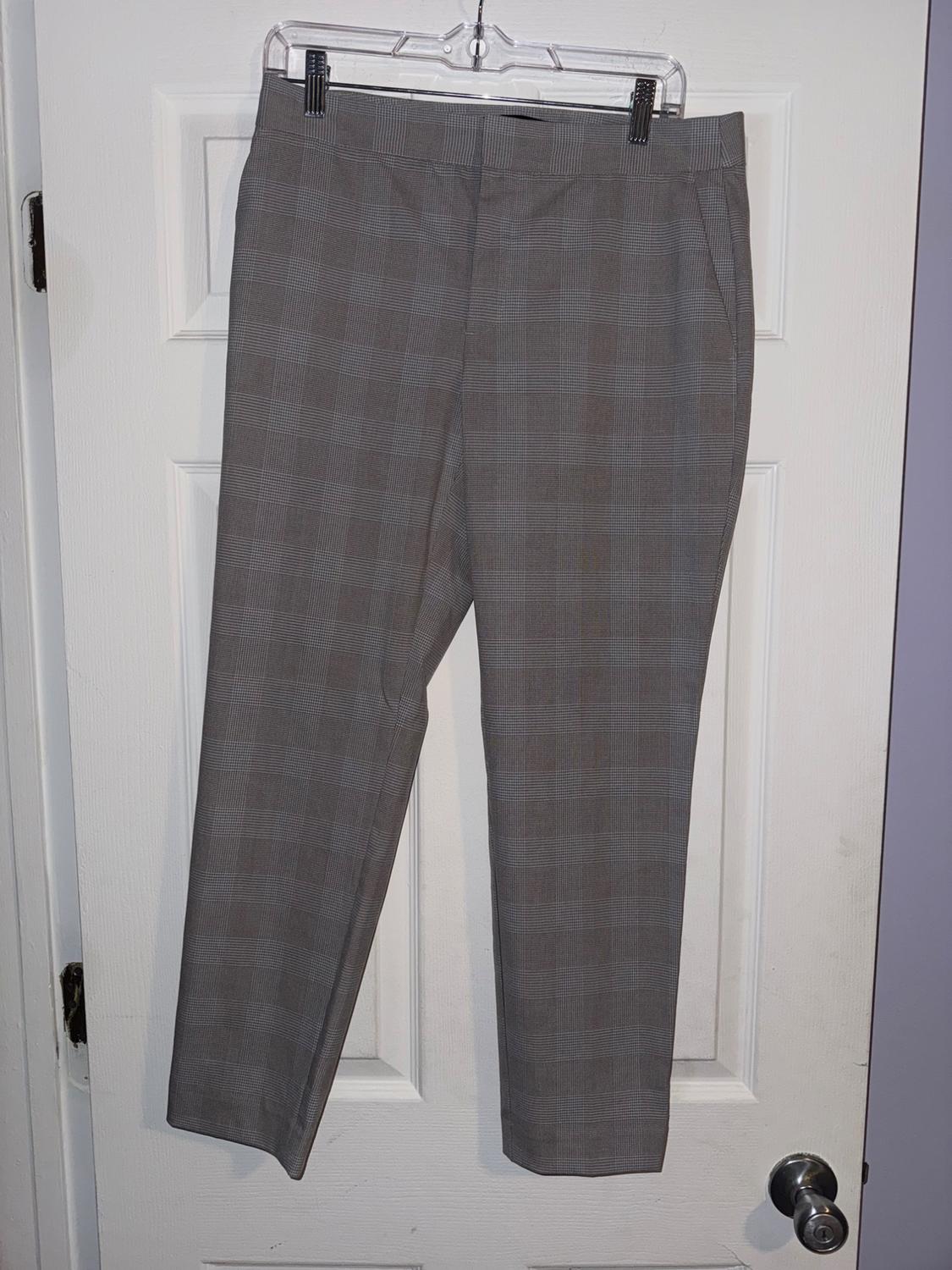 Grey checked trousers hanging on a clear hanger over a white door.