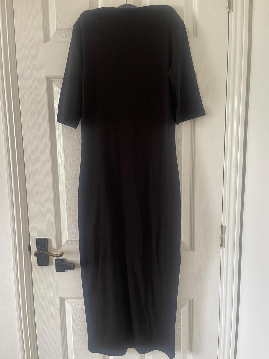 Short-sleeved black maxi dress hanging on a white interior door with a dark handle.