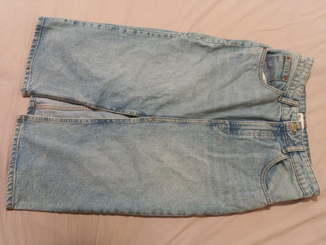 Light blue denim skirt on a beige surface, with button and zip fastening, casual and relaxed style.