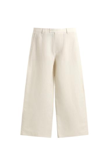 Front view of light beige relaxed fit trousers, front pleats, side and jetted back pockets, zip and button fastening.