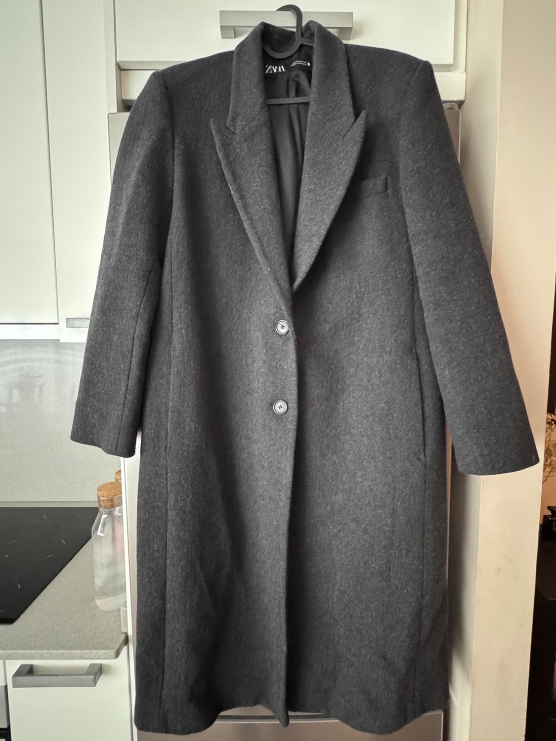 Dark grey coat hanging on a hanger, with wide lapels and two buttons, in a modern kitchen setting.