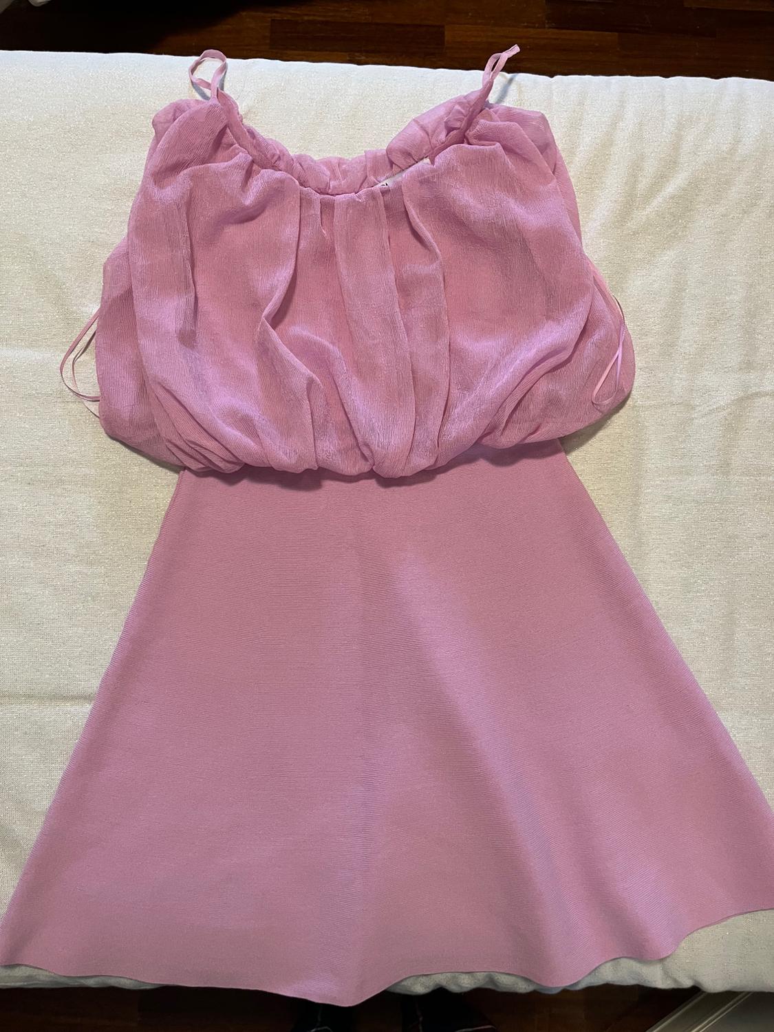 Pink sleeveless dress with spaghetti straps, ruched bodice, and flared skirt, on a light surface.