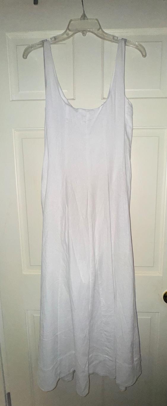 Sleeveless white dress hanging on a clear hanger in front of a white door.