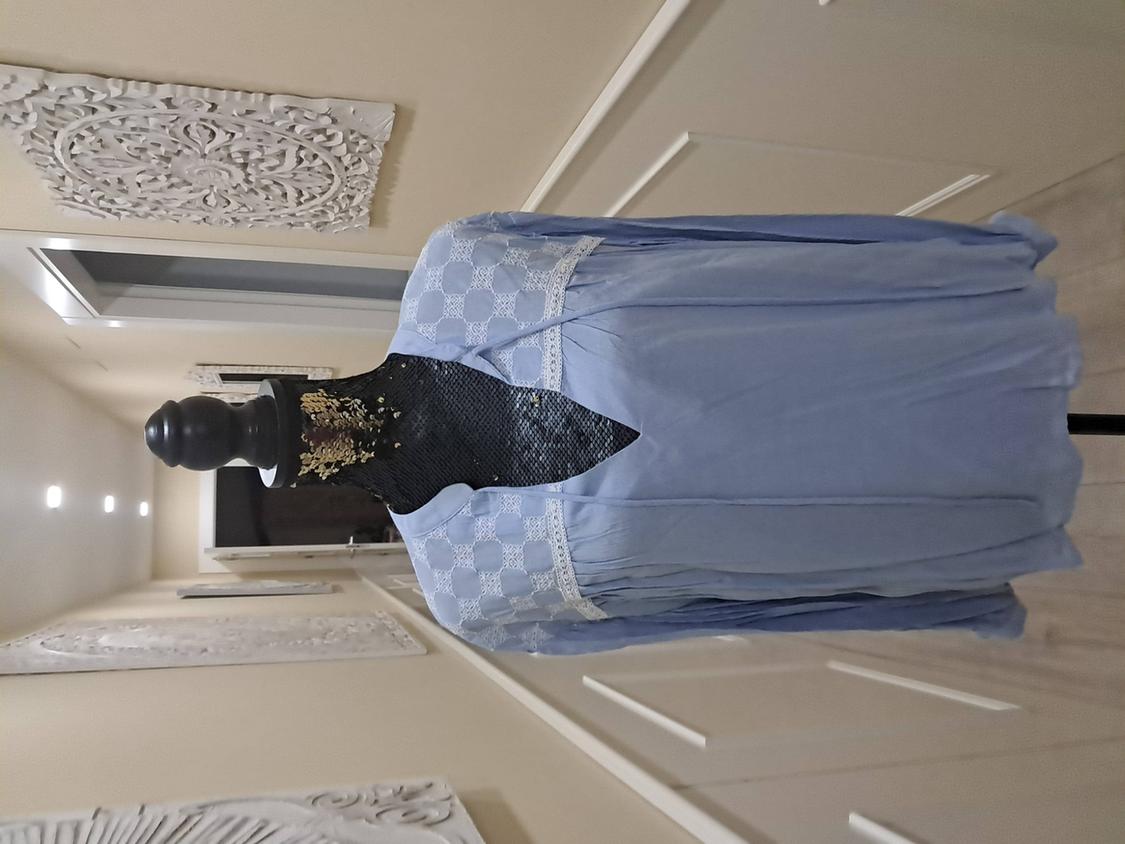 Mannequin with a light blue lace-shoulder blouse, in a hallway with carved panel decoration on the wall.