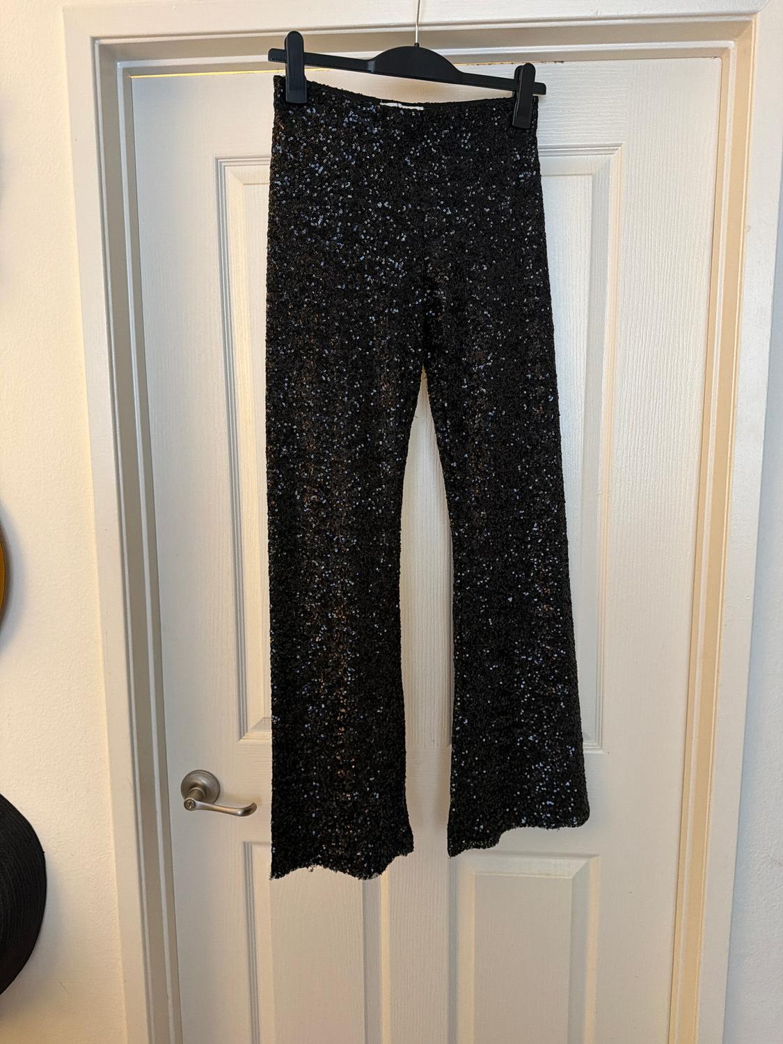 Black sequined pants hanging on a black hanger over a white door. Lit indoor environment.