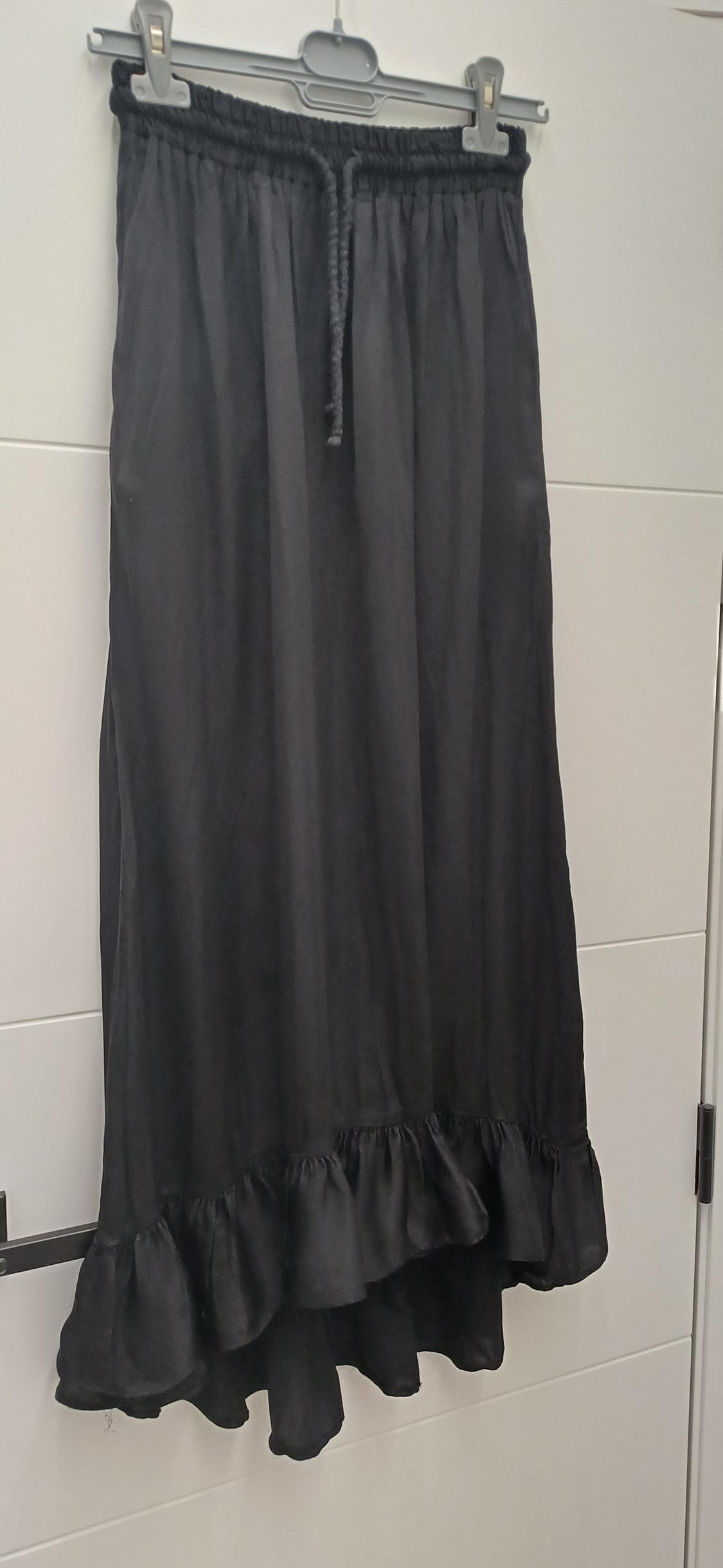 Long black skirt with an elasticated drawstring waist, hanging on a hanger. It has a frill on the bottom hem.