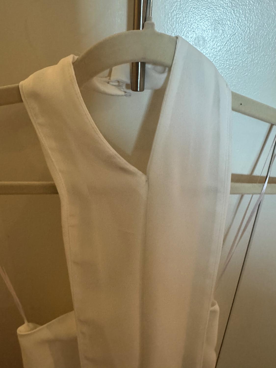 White dress hanging on a wooden hanger, with a light-coloured wall in the background. The fabric appears soft and light.