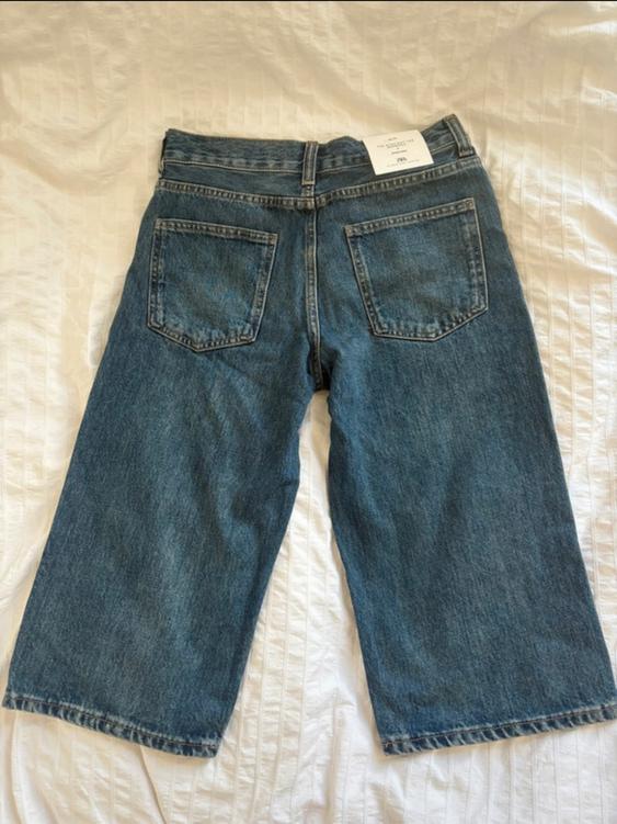 Wide blue denim jeans with back pockets, on a white bedspread. Visible label on the waistband.