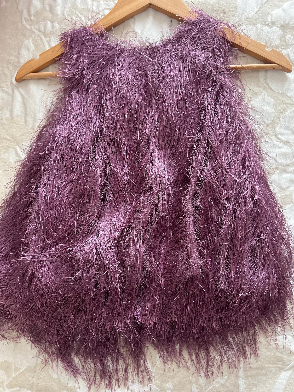 Sleeveless, furry-textured purple dress, hanging on a wooden hanger against a light background with a floral design.