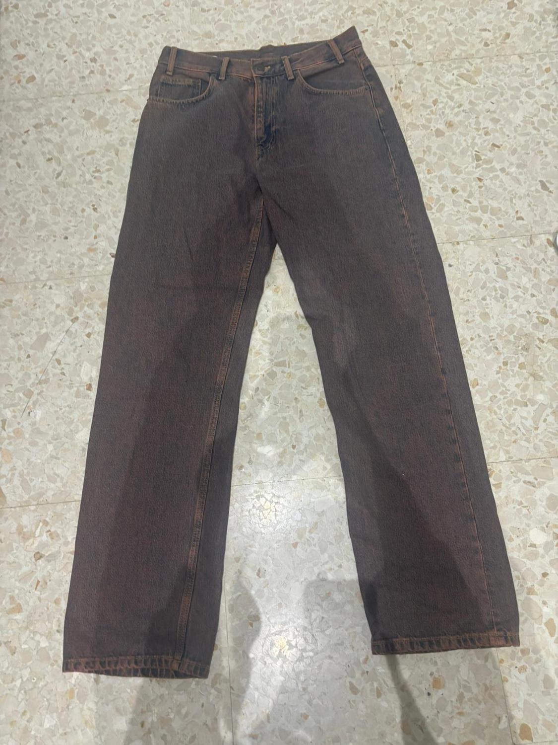 Straight-cut brown jeans on a light tiled floor, viewed from above.