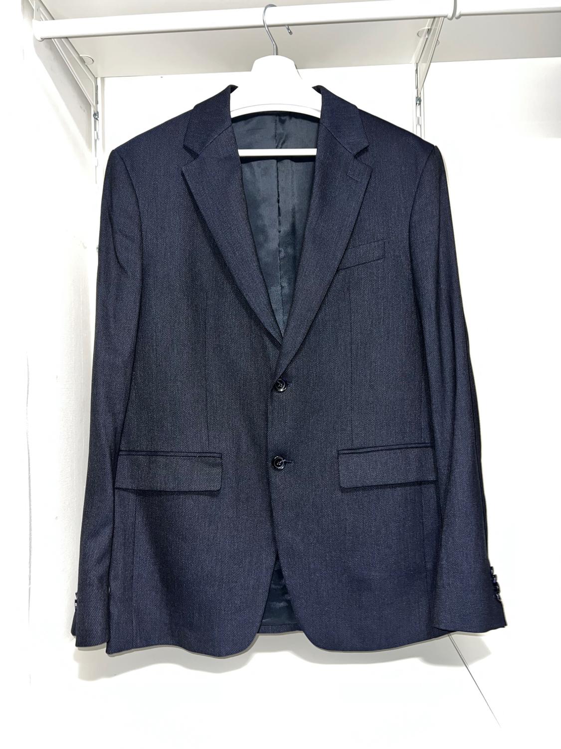 Dark blue suit jacket hanging on a white hanger, with two buttons and front pockets, on a white background.