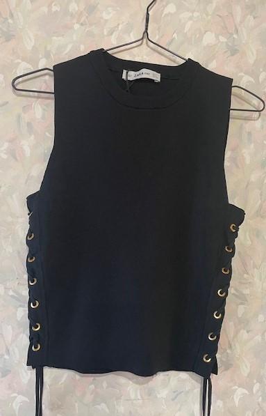 Black sleeveless top with gold eyelets on the sides, hanging on a hanger against a light floral background.