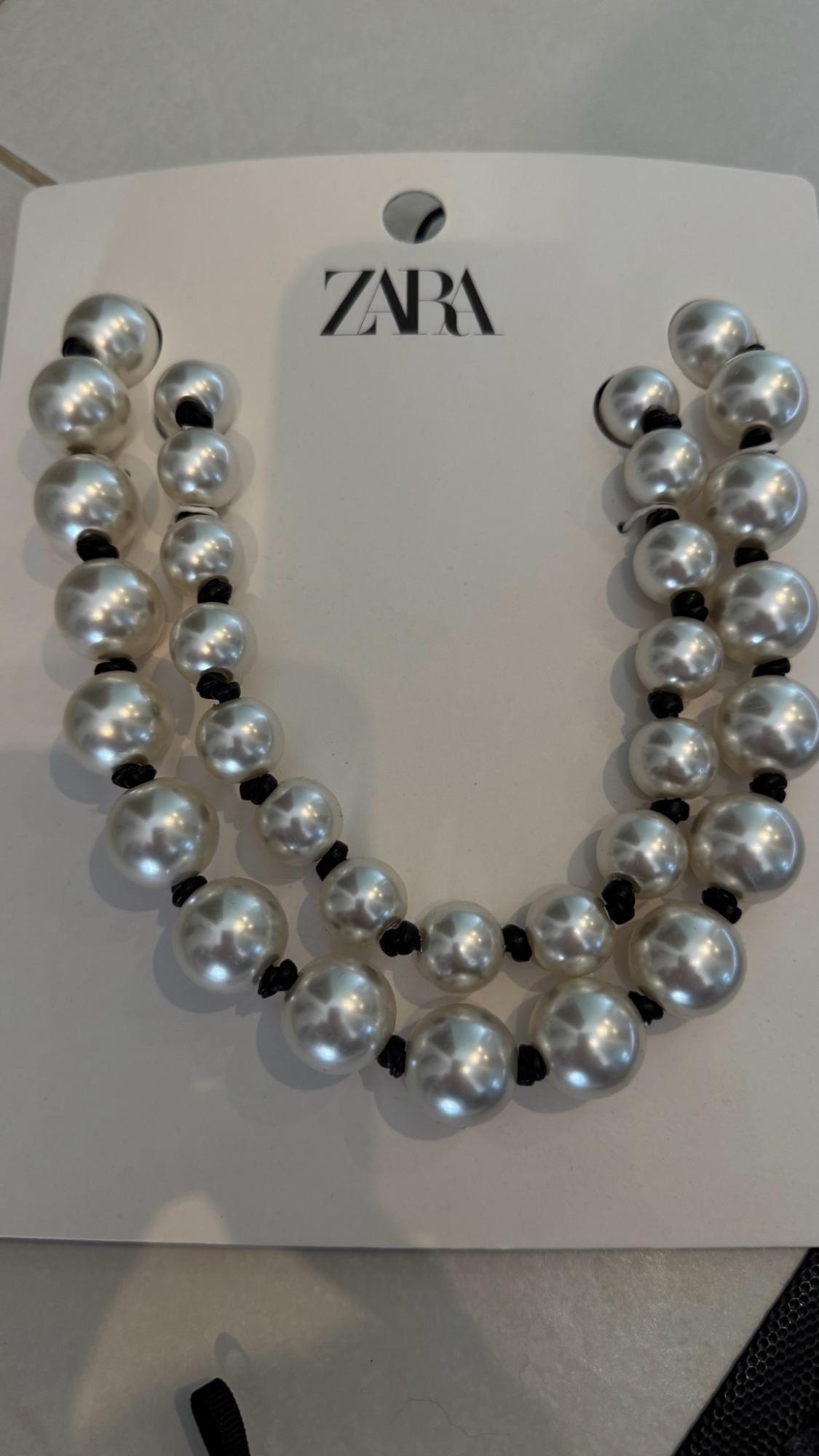 Close-up of a double-strand white pearl necklace with black knots on card featuring the text Zara.