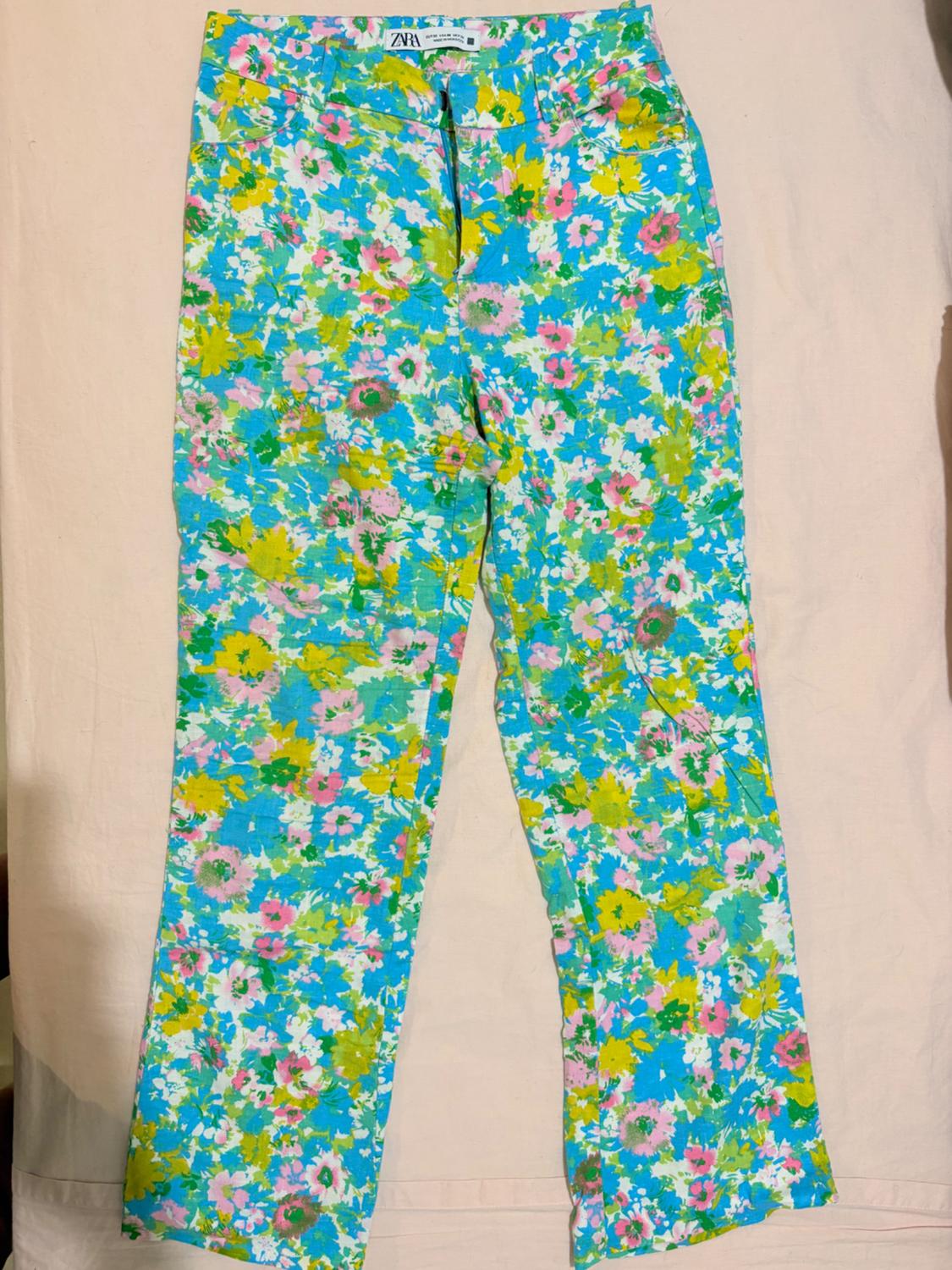 Trousers with a floral print in blue, green, yellow, and pink tones on a light background. ZARA text on the label.