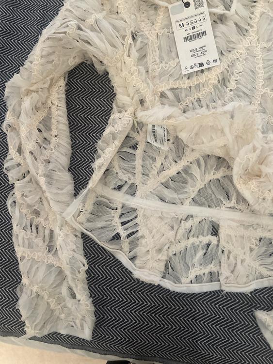 White fabric with lace texture on a blue zigzag pattern background. Visible tag with price of $69.90 and size M.