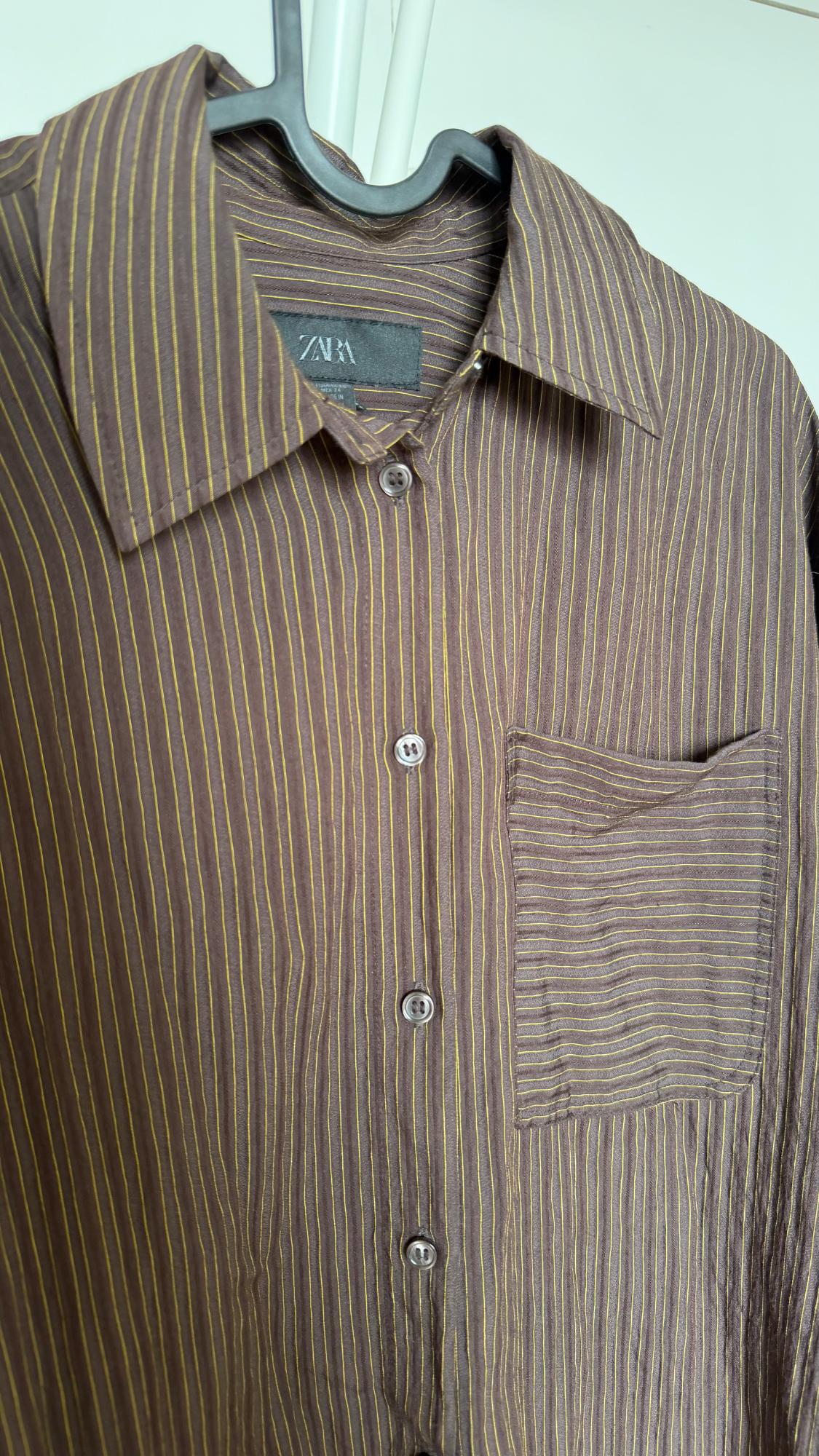 Brown shirt with yellow vertical stripes on a hanger. Pocket with horizontal stripes and a label on the collar with the text Zara.