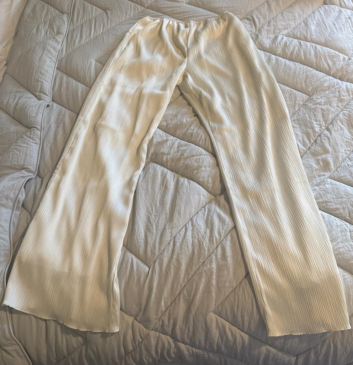 White pleated fluid trousers on a grey quilted duvet, conveying a casual and relaxed style in a home setting.