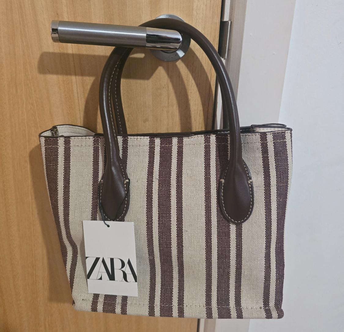 Brown and beige striped handbag hanging on a door handle, with visible Zara tag.