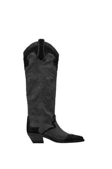 Side view of a grey high boot with embroidered design and a low, wide heel.
