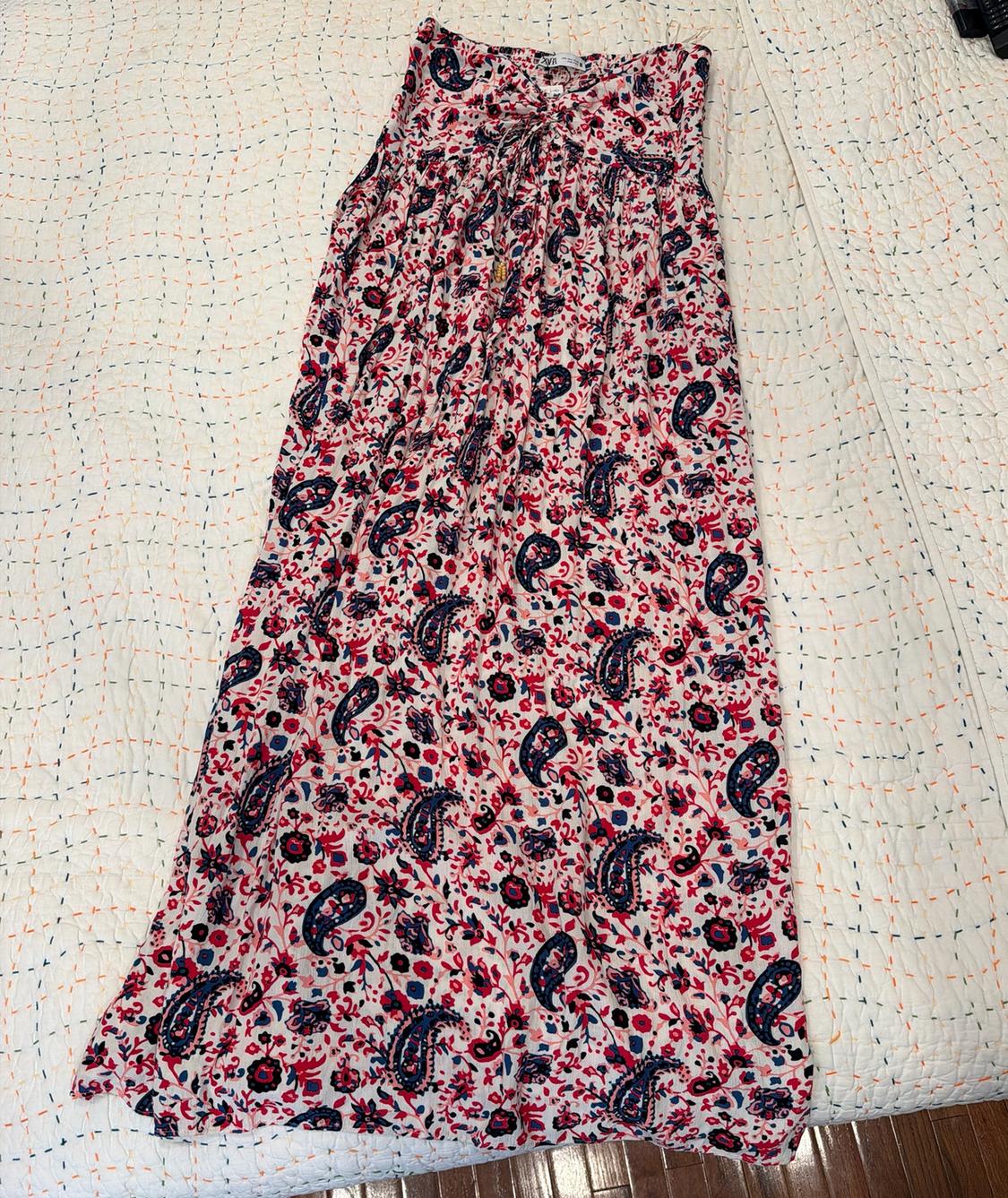 Sleeveless maxi dress with a red and blue paisley print, laid out on a white bedspread.