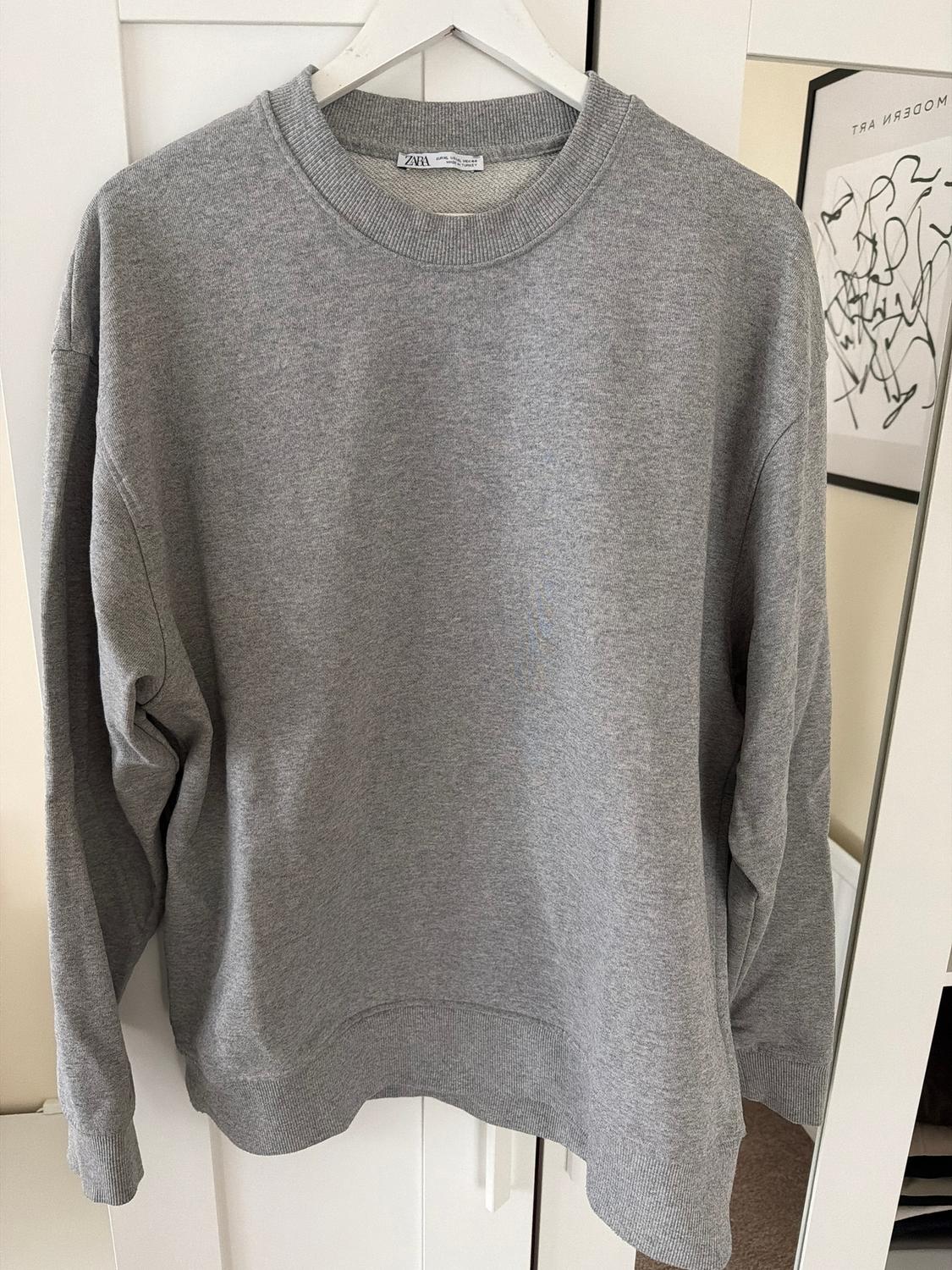 Grey sweatshirt hanging on a white hanger in front of a wardrobe. In the background, a picture with abstract modern art.
