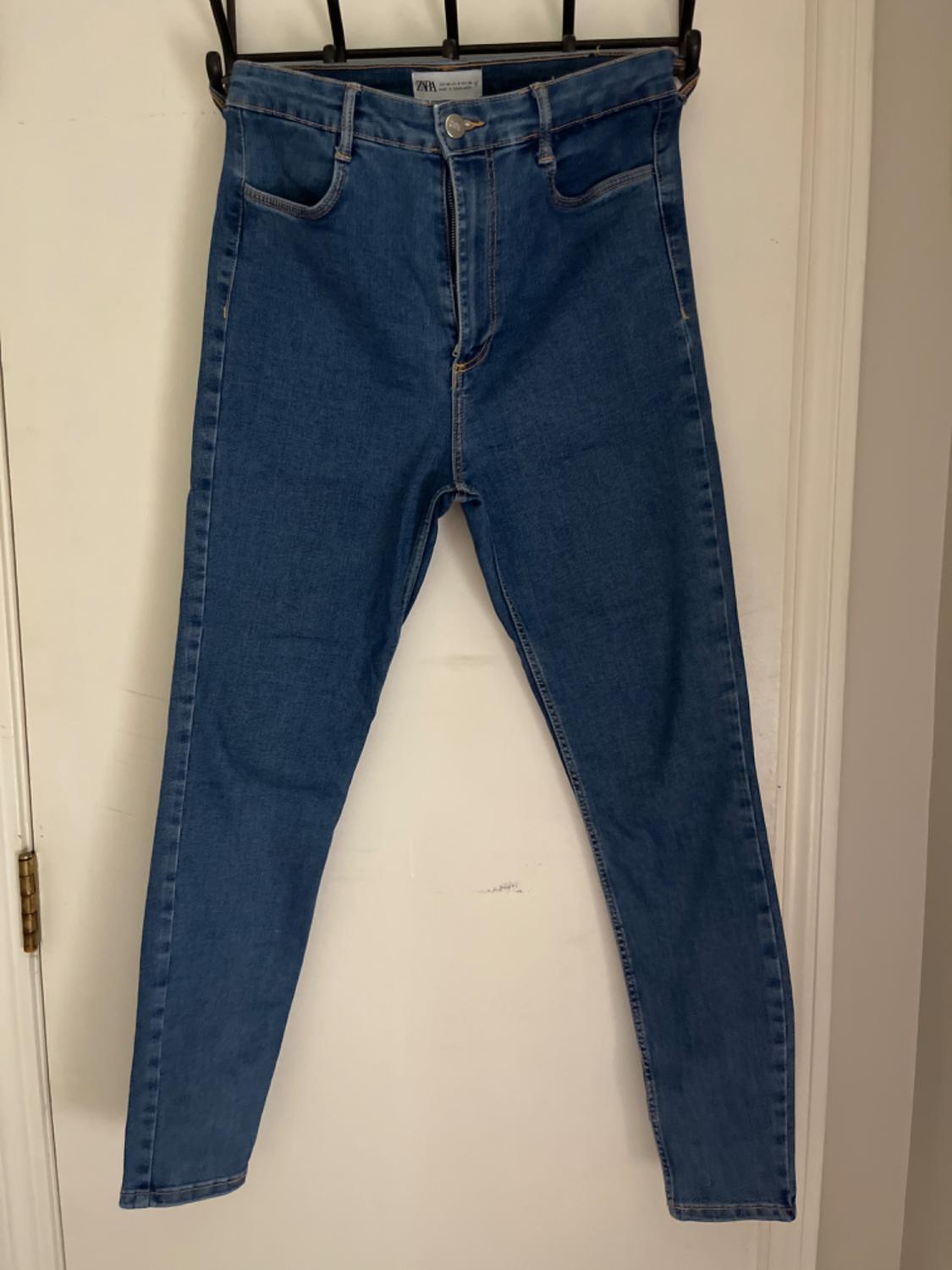 Front view of blue denim jeans with front pockets and button fastening.