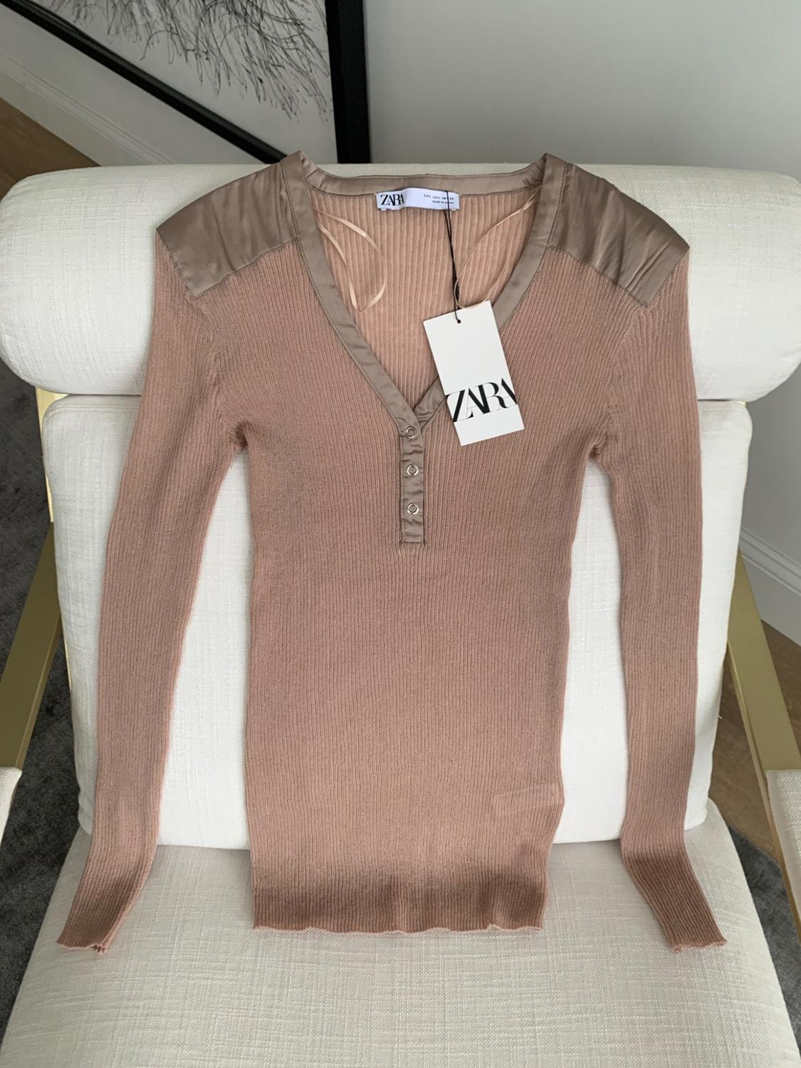 Pink ribbed knit top with long sleeves, a V-neck, buttons and satin panels. ZARA label. Photograph on a white chair.