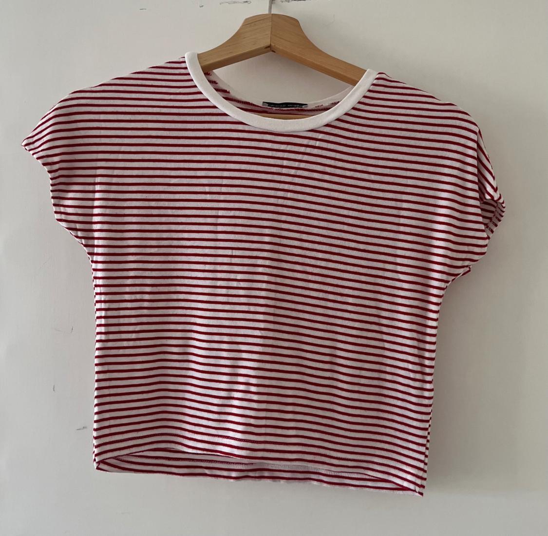 Casual short-sleeved red and white horizontal striped T-shirt, hanging on a wooden hanger against a white wall.
