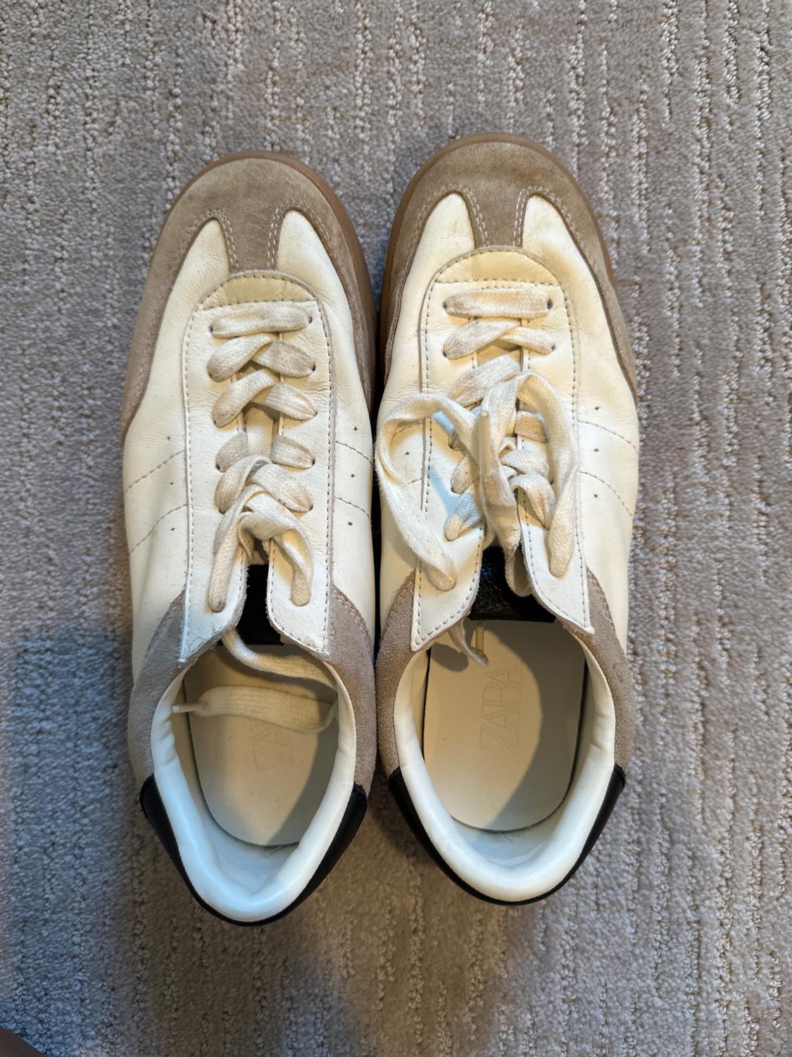 White and beige sneakers with laces on a gray carpet. Interior visible with insole that has the text "ZARA".