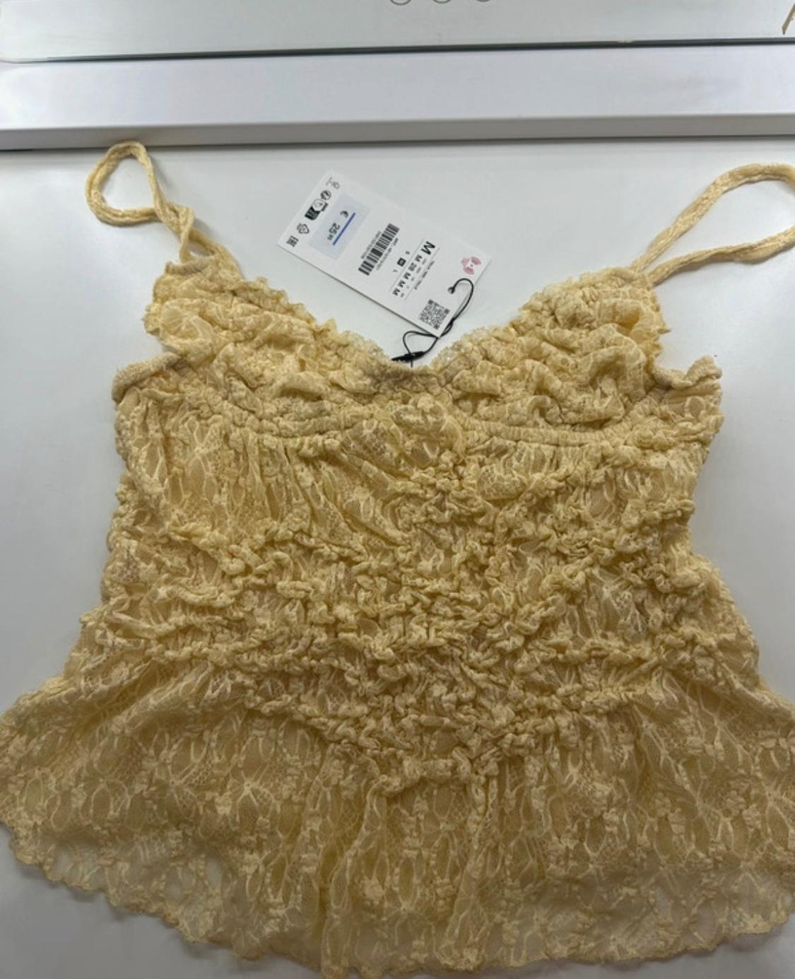 Light yellow lace camisole with thin straps and a gathered texture on a white surface. Label with the text € 25.