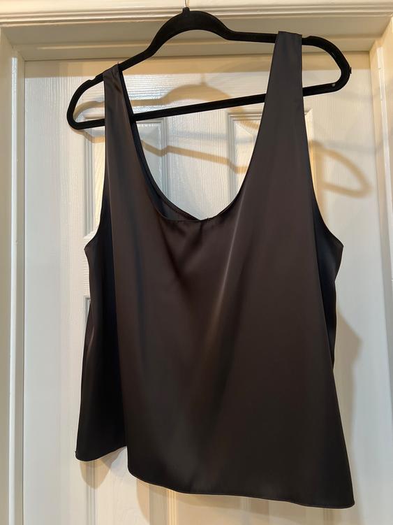 Sleeveless black blouse hanging on a black hanger over a white door. The fabric appears soft and flowing.