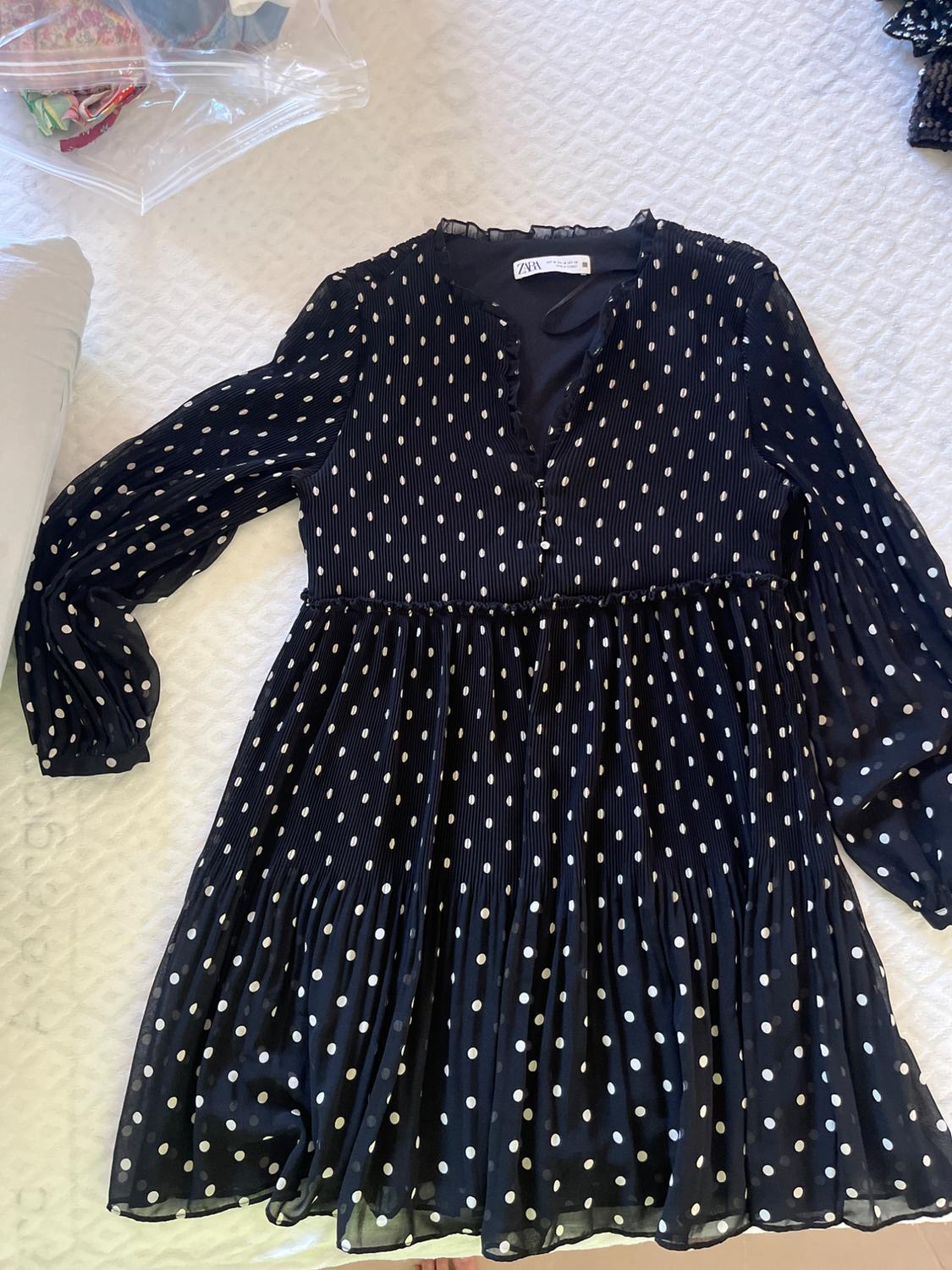 Black pleated dress with white polka dots and long sleeves on a white surface. Label with the text ZARA visible at the neckline.