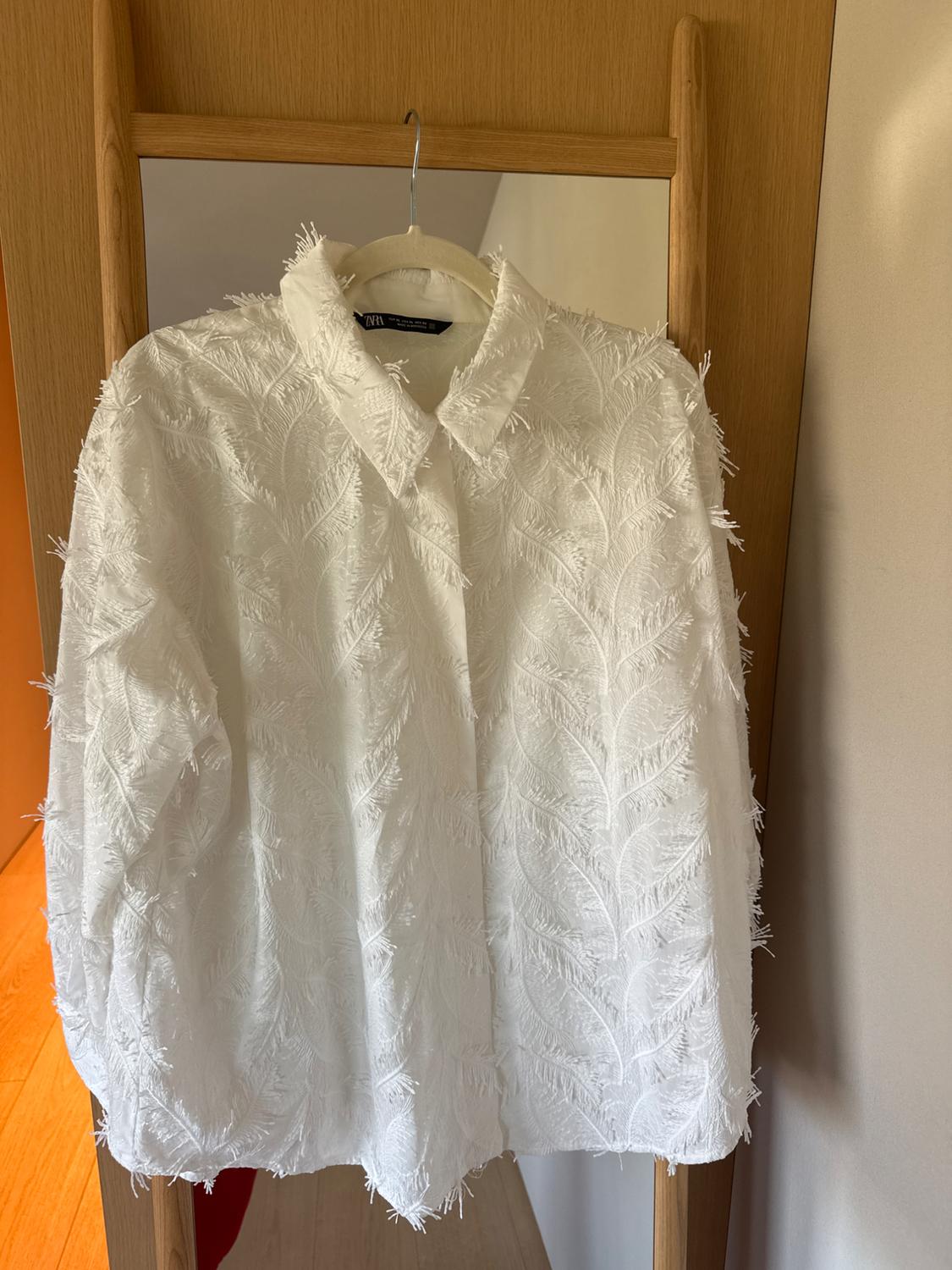 White feather-textured shirt hanging on a wooden mirror. Light wall and wooden floor background.