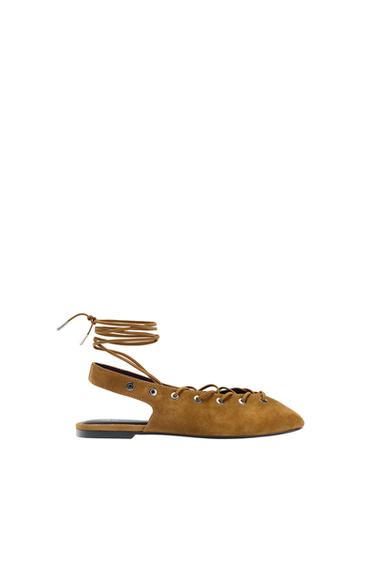 Brown flat shoe with long laces to tie around the ankle, black sole, and metallic eyelets, on a white background.
