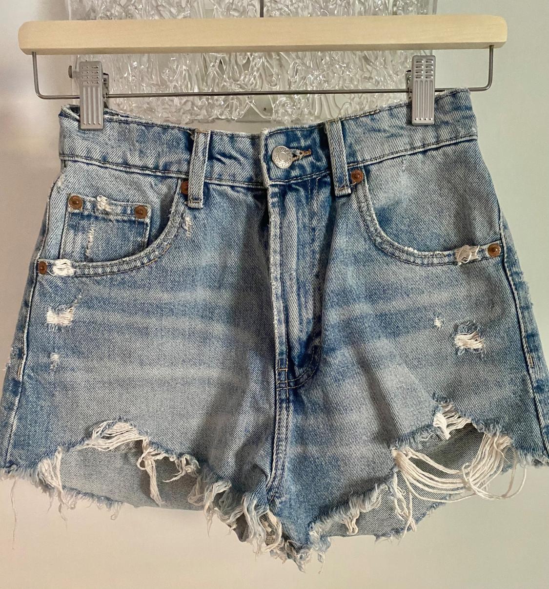 Front view of distressed denim shorts with front pockets and a frayed hem.