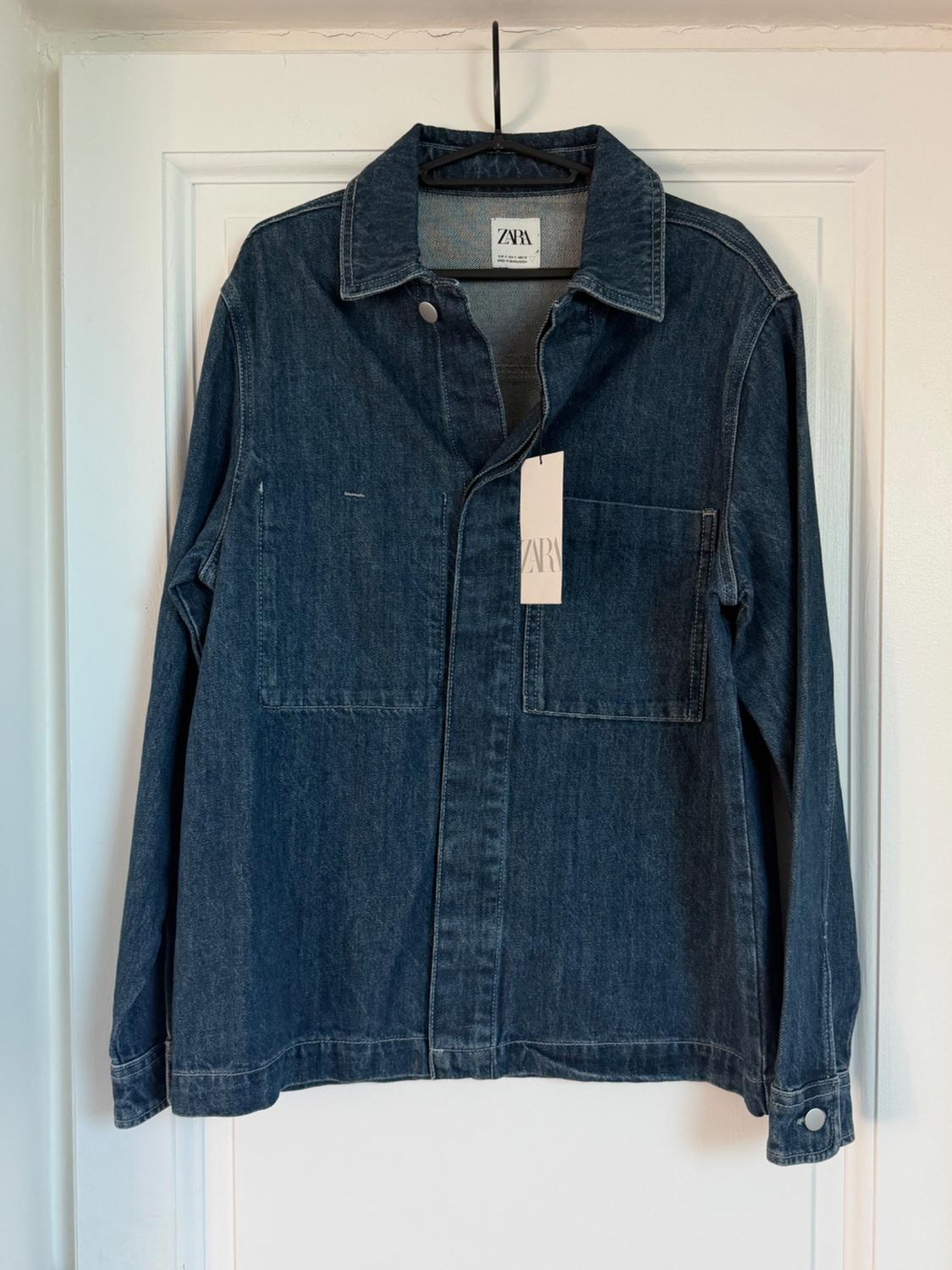 Blue denim jacket hanging on a white door, with visible label that reads "ZARA".
