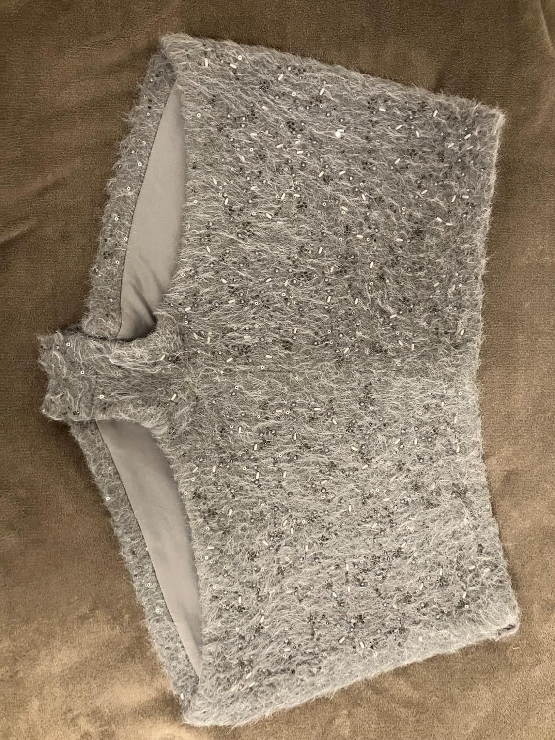 Grey fluffy knit shorts with sequins, photographed on a textured brown surface.