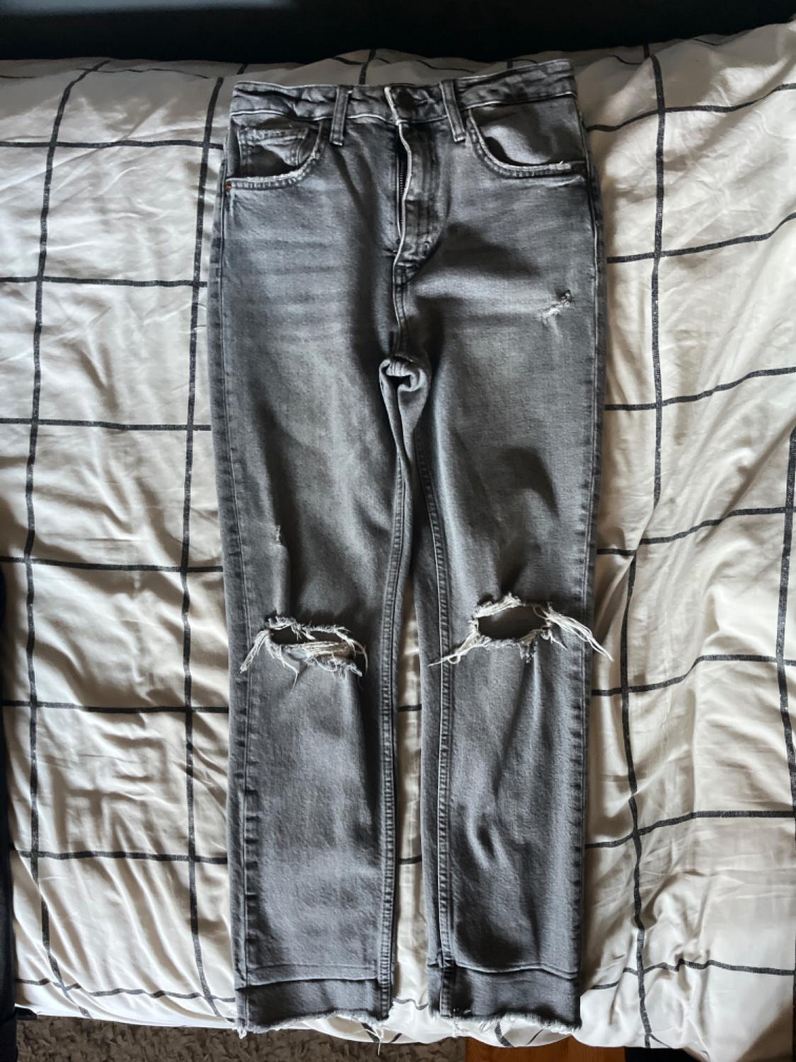 Front view of gray pants with ripped knees and front pockets.