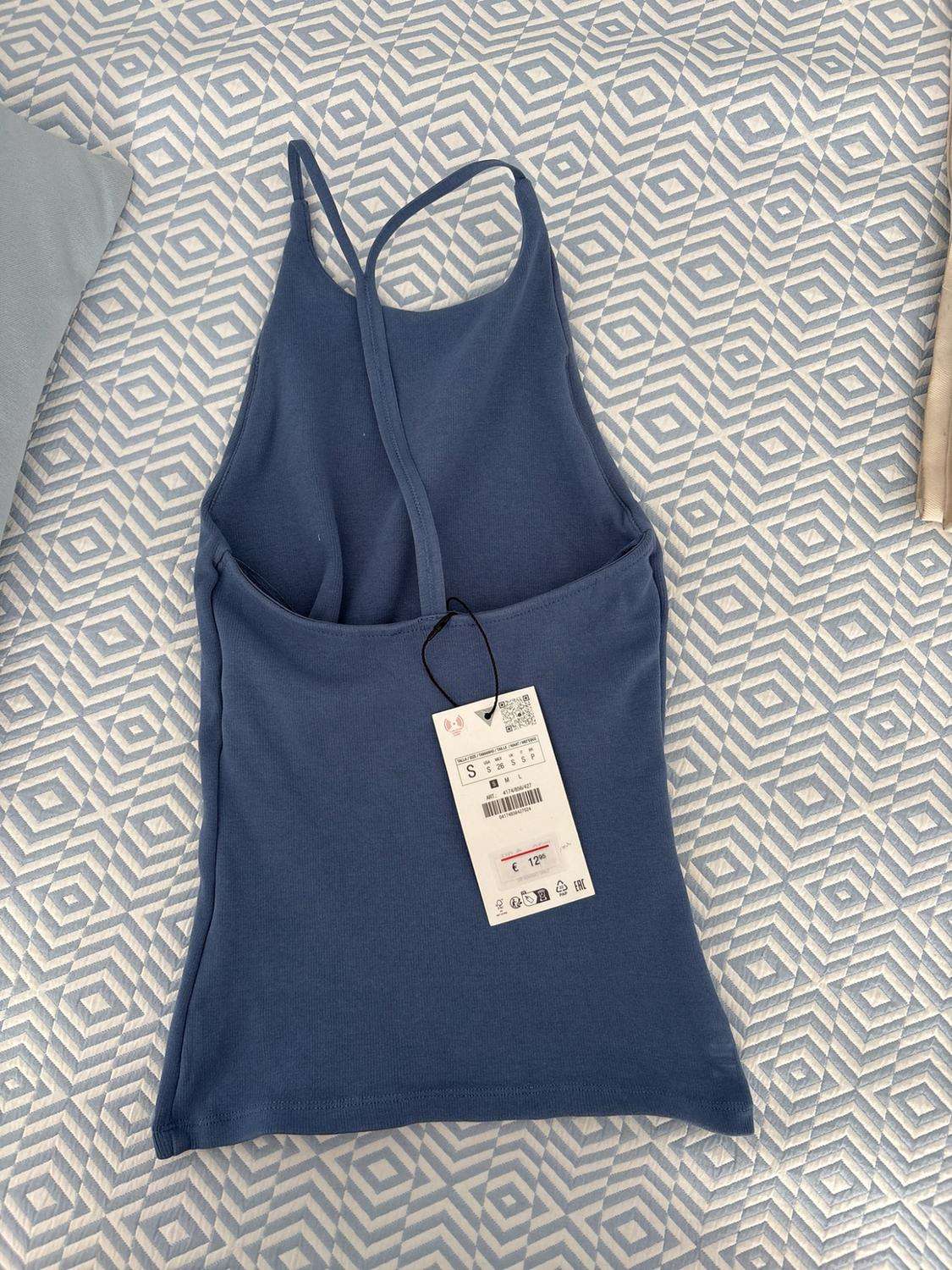 Blue ribbed strappy top over fabric with a geometric print. Label with the text S and €12.95.