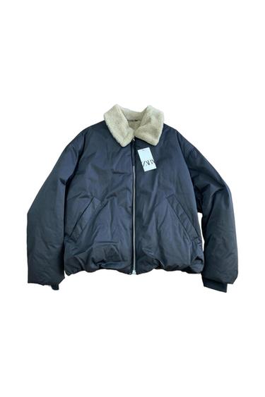 Black jacket with zipper and beige wool collar. Visible label with the text "ZARA". White background.