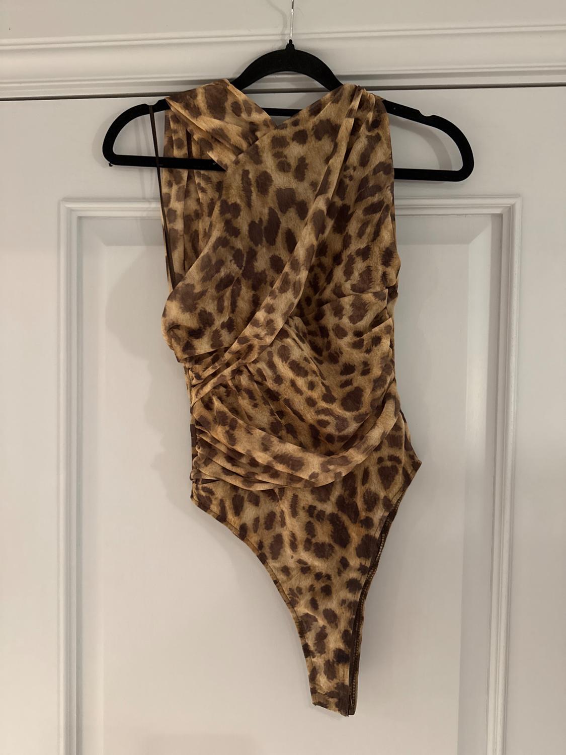 Animal print bodysuit in brown tones hanging on a black hanger over a white door.