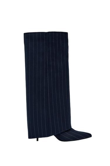 Μπότα με τακούνι σε σκούρο μπλε (navy blue) χρώμα με λευκή ριγέ (pinstripe) λεπτομέρεια. Σχedίο με φαρδιά, επικάλυπτη ψηλή μπότα και μυτερή μύτη, σε λευκό φόντο.