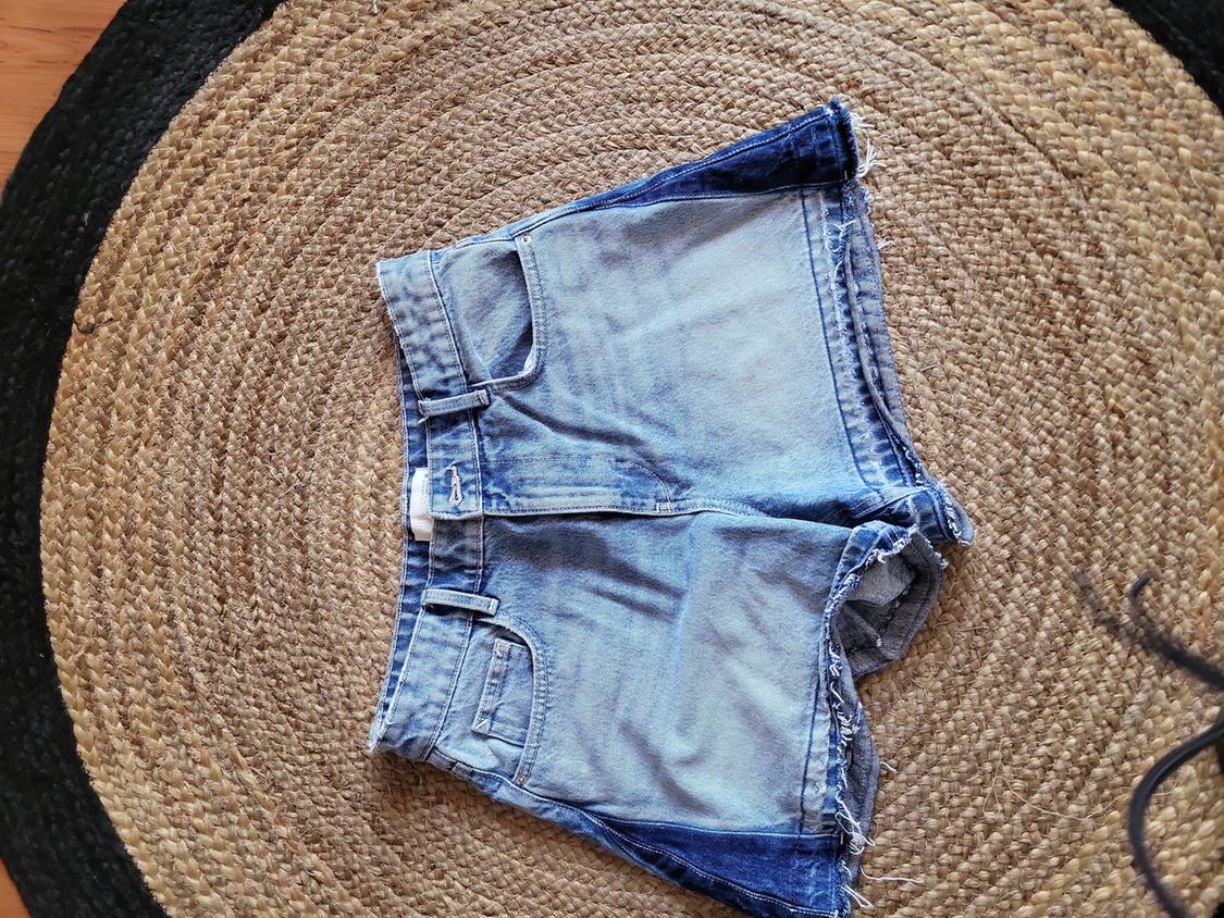 Light blue denim shorts with frayed edges, placed on a round jute rug in shades of brown and black.